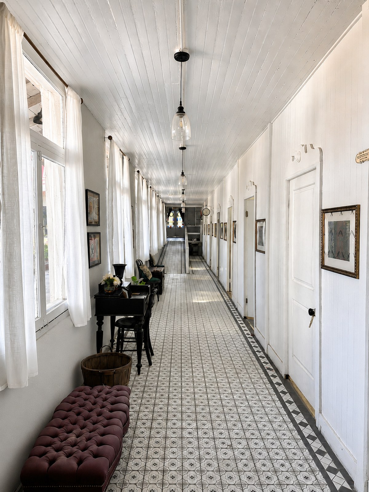 A long interior hallway at The Crescent House paved in patterned Victorian style tile, lined with white doors and framed pictures